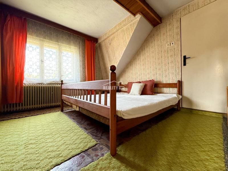 A bedroom in a family house with a wooden bed, orange curtains, and a green carpet.