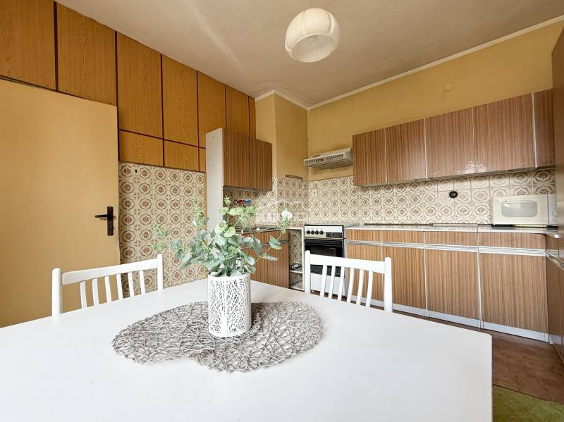 A kitchen in a family house with retro tiles, a kitchen unit, and a white table with a plant.