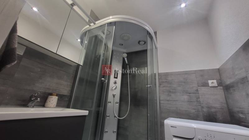A bathroom in a studio apartment with a massage shower cabin and a washing machine.