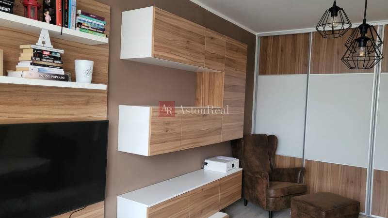 Interior of a 1-room apartment with wooden furniture, a television, and shelves with books.