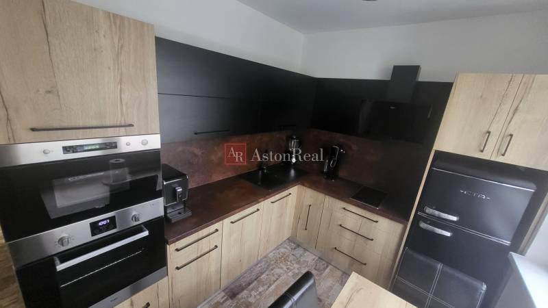 A kitchen in a studio apartment with wooden cabinets and modern appliances.