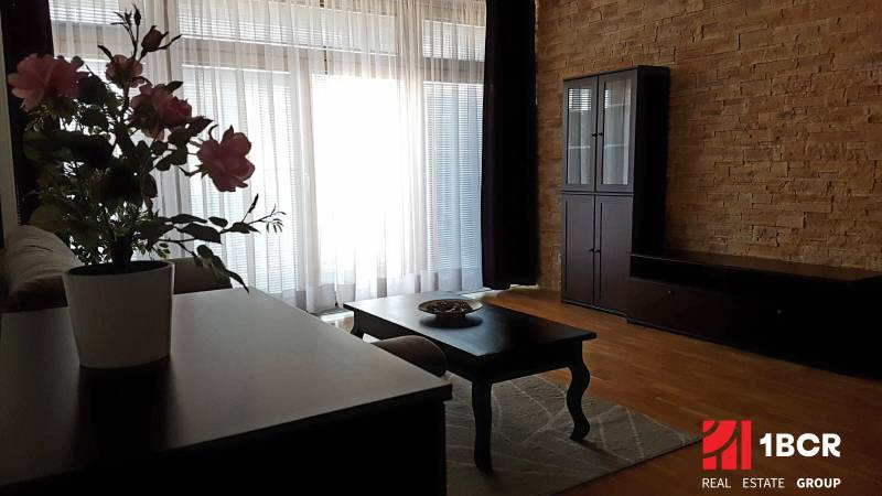 Living room in a two-room apartment with brick walls and wooden furniture, decorated with flowers.