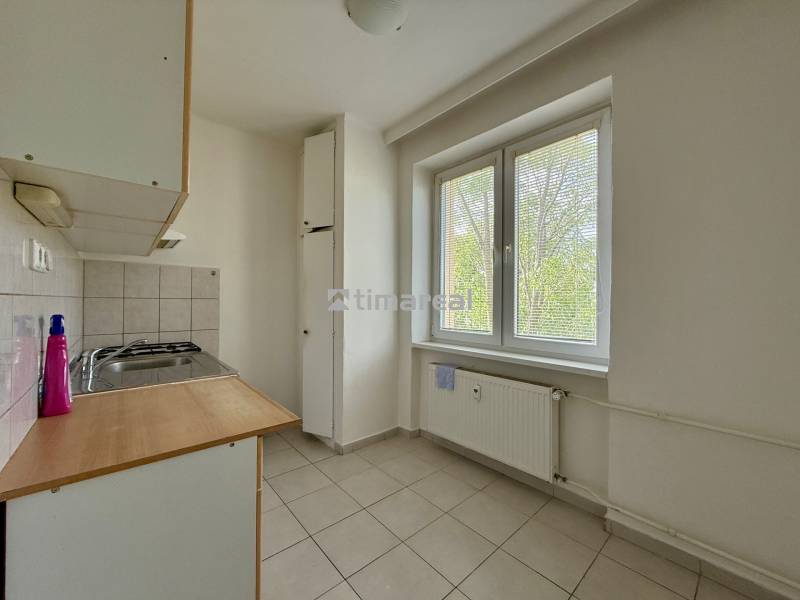 A kitchen with a window and a radiator in a 2-room apartment, light tiles and basic equipment.