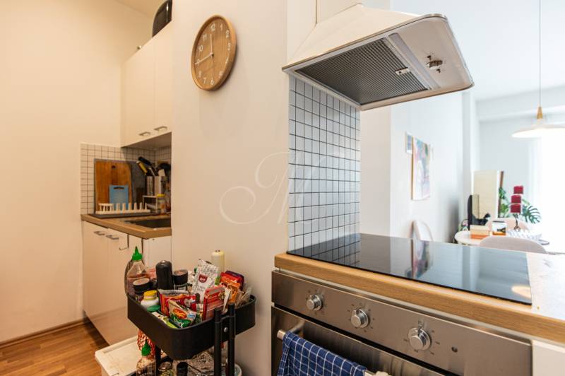 A kitchen with a cooktop and a range hood in a two-room apartment, complemented by a clock and kitchen utensils.