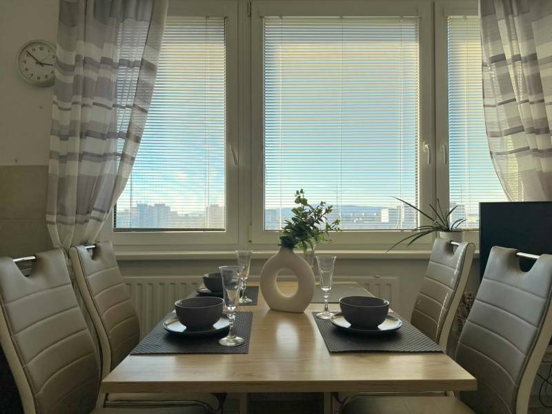 Dining table with placemats, four chairs, and a view of the city from a 2-room apartment.