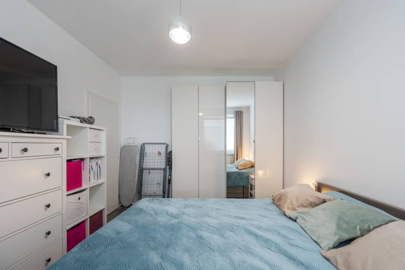 A bedroom with a bed, wardrobe, dresser, and television in a two-room apartment.