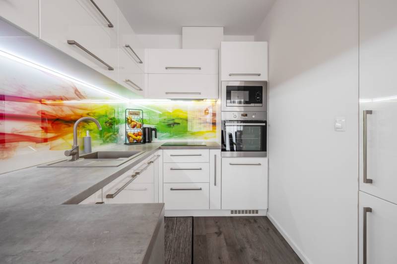 A kitchen in a 2-room apartment with a colored glass backsplash and built-in appliances.