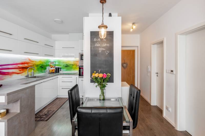 A kitchen in a 2-room apartment with a colored glass panel and a glass table with a vase of flowers.