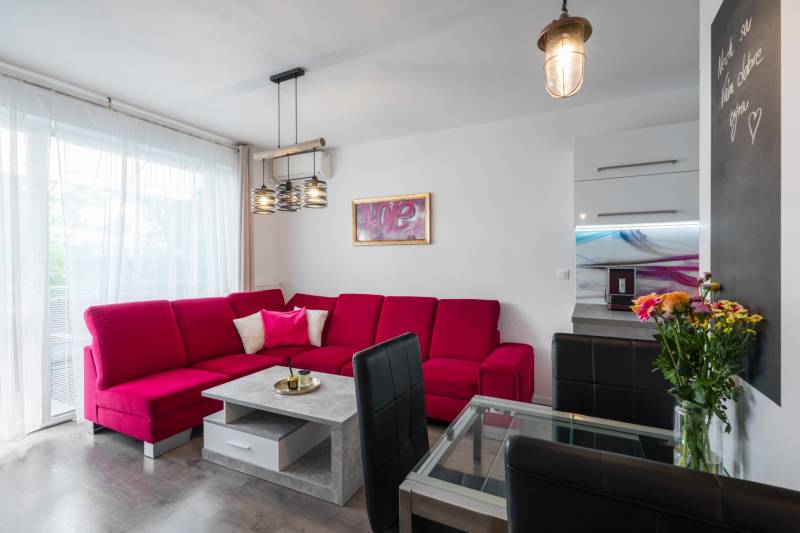 Living room in a two-room apartment with a red sofa, glass table, and flowers.