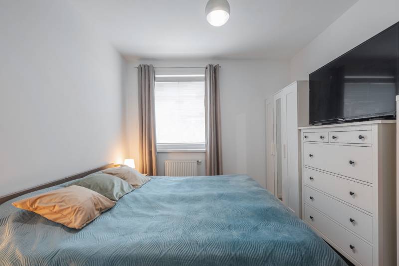 Bedroom in a 2-room apartment with a light bed, wardrobe, and a TV on a dresser.