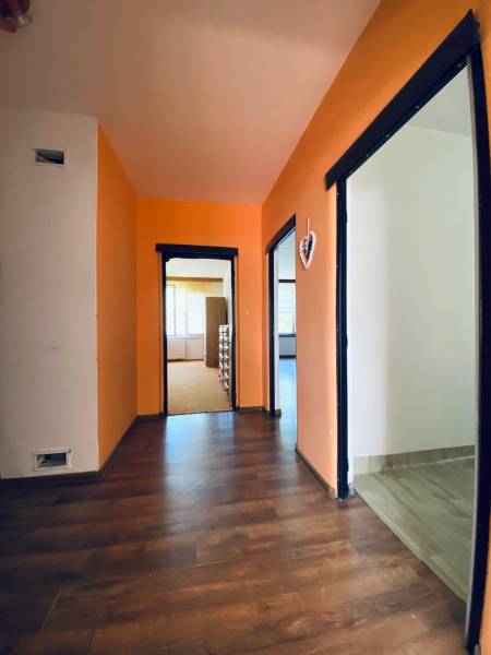 A hallway in a 4-room apartment with orange walls and a dark floor.