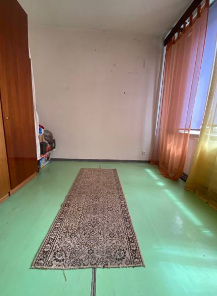A spacious room with a green floor, carpet, and colorful curtains in a 4-room apartment.