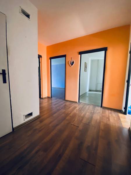 Interior of a 4-room apartment with an orange wall and wooden flooring, three open rooms.