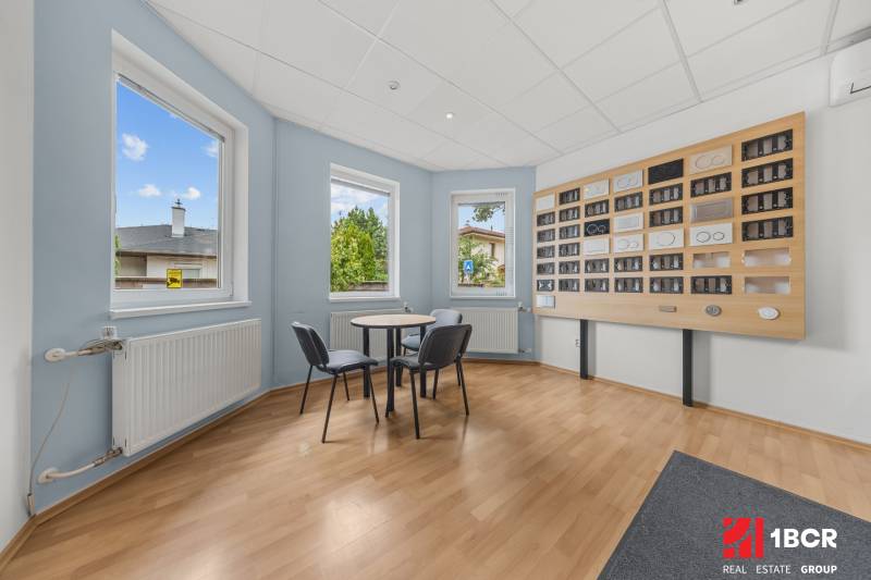 A room in a family house with windows, a table, and chairs by the wall with frames.