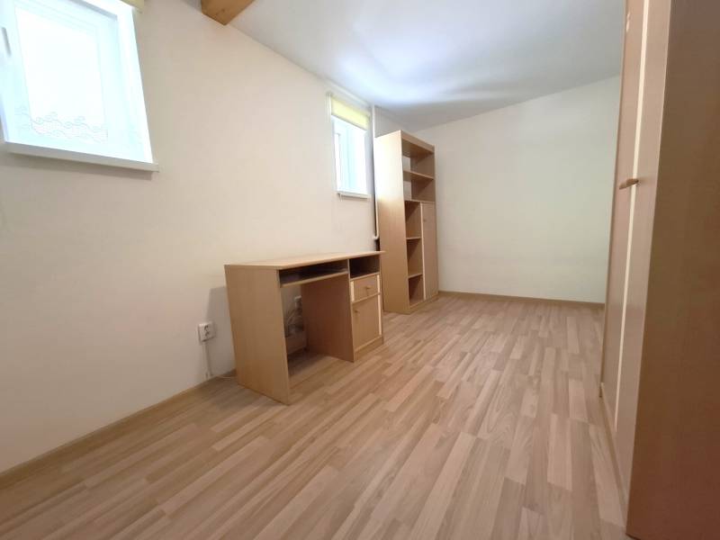 A room in a 4-room apartment with wooden flooring, a writing desk, and shelves.