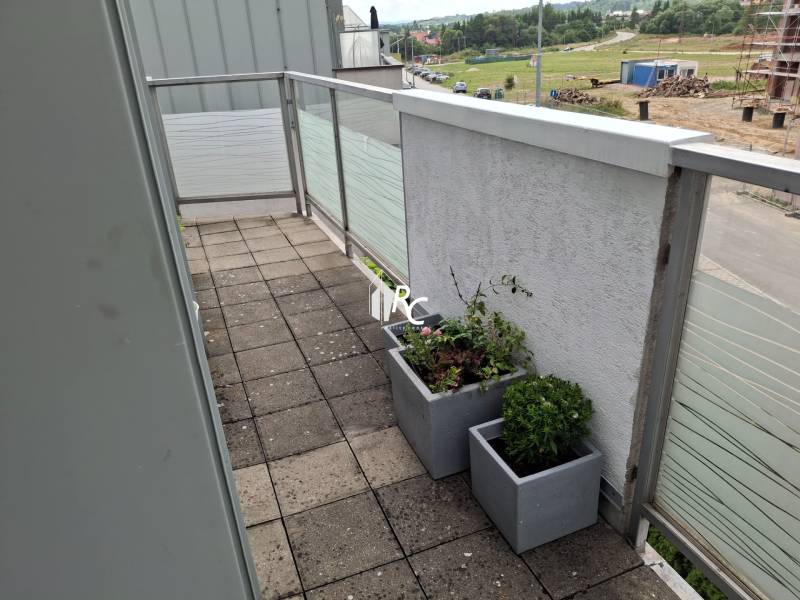 A balcony in a 4-room apartment with flower pots and a view of the outskirts of the city of Martin.