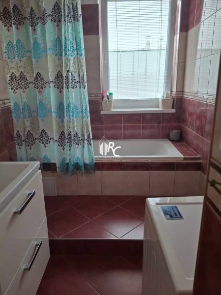 A bathroom in a 4-room apartment with a bathtub, curtain, washing machine, and window.