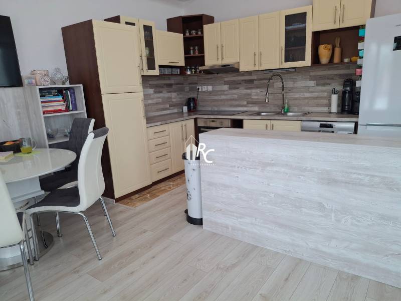 A kitchen in a 4-room apartment with a dining table, light wood, and white cabinets.