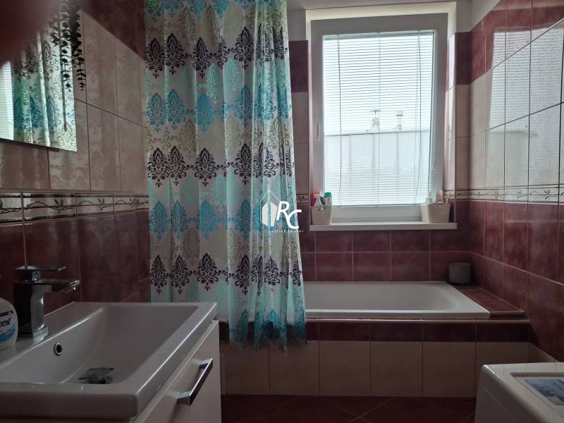 A bathroom with a curtain and a bathtub, tiles in brown shades, a bright window, a 4-room apartment.