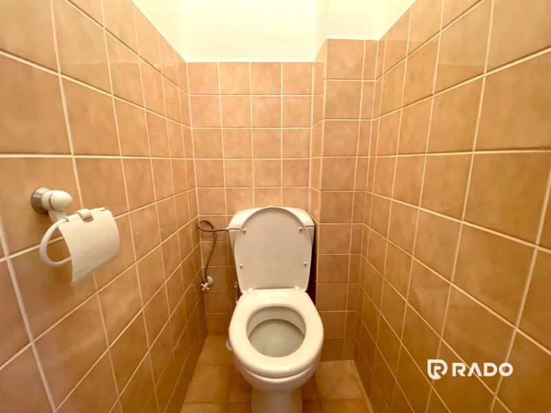 A toilet in a 2-room apartment with beige tiles and a toilet paper holder.