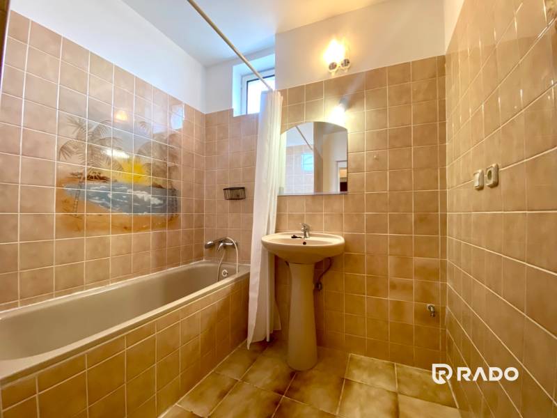 Bathroom with a bathtub, sink, and a picture of a beach on the tiles in a 2-room apartment.