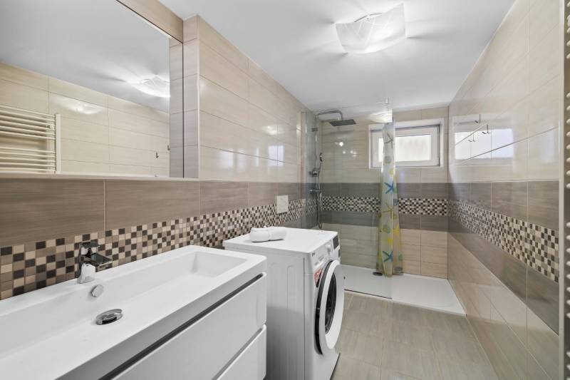 Bathroom with a washing machine, shower, and sink, on Pluhova Street in a family house, light tiles.