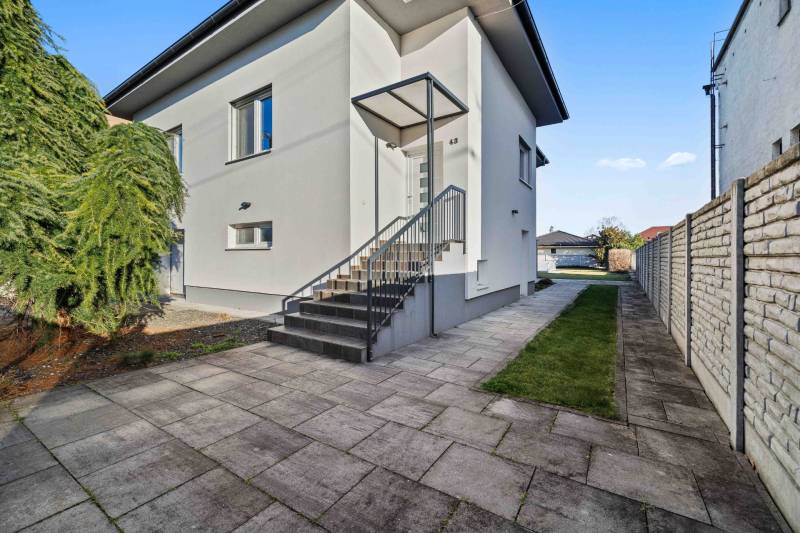 Family house on Pluhová Street, next to a sidewalk with concrete tiles and shrubs.