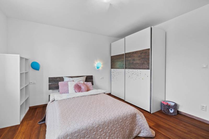 Bedroom with a bed, wardrobe, and lamp, Pluhová, in a family house with wooden flooring.