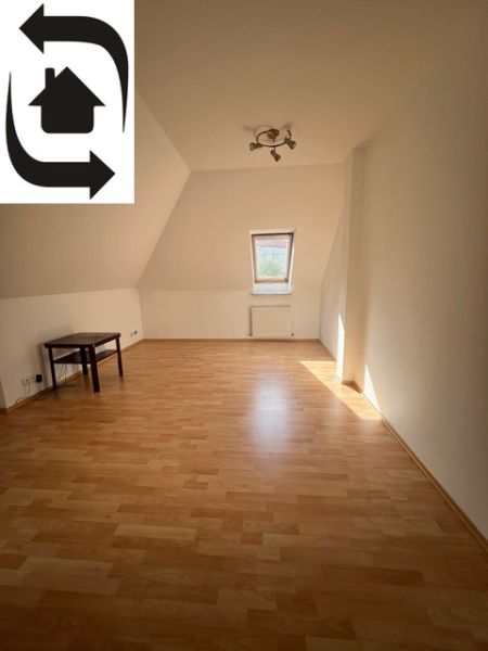 Room with a slanted ceiling, wooden decor floor, table, well-lit.