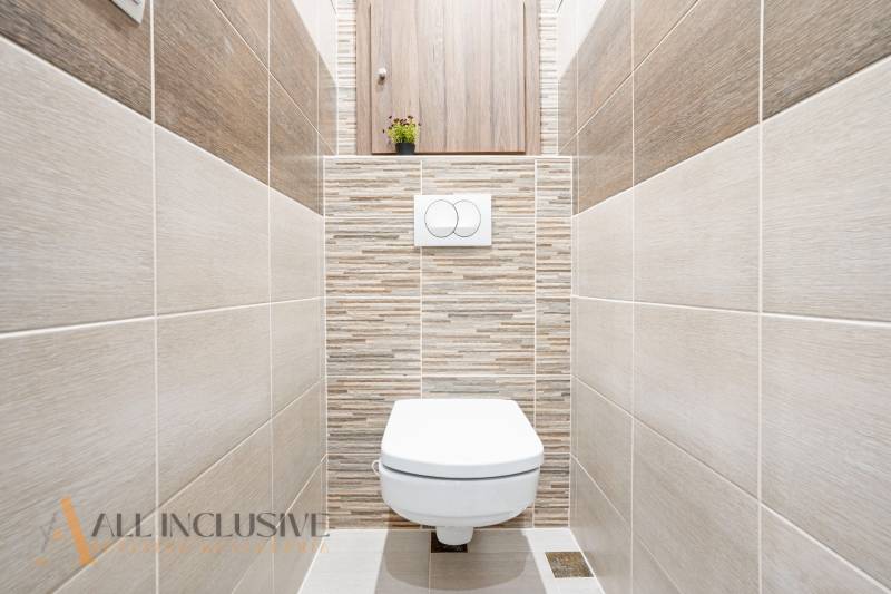 A toilet in a 3-room apartment with tiles in neutral shades.