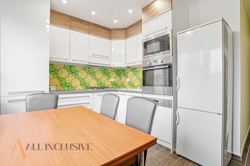 A kitchen in a 3-room apartment with colorful tiles, a white refrigerator, and a wooden table.