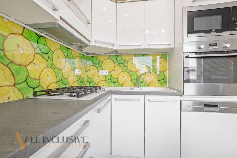 A kitchen in a 3-room apartment with colorful fruit tiles and modern appliance equipment.