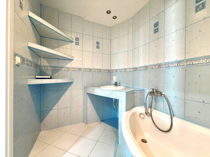 A bathroom in a 3-room apartment with a corner bathtub and wall shelves.