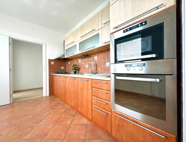 A kitchen of a 3-room apartment with brown tiles and built-in appliances.