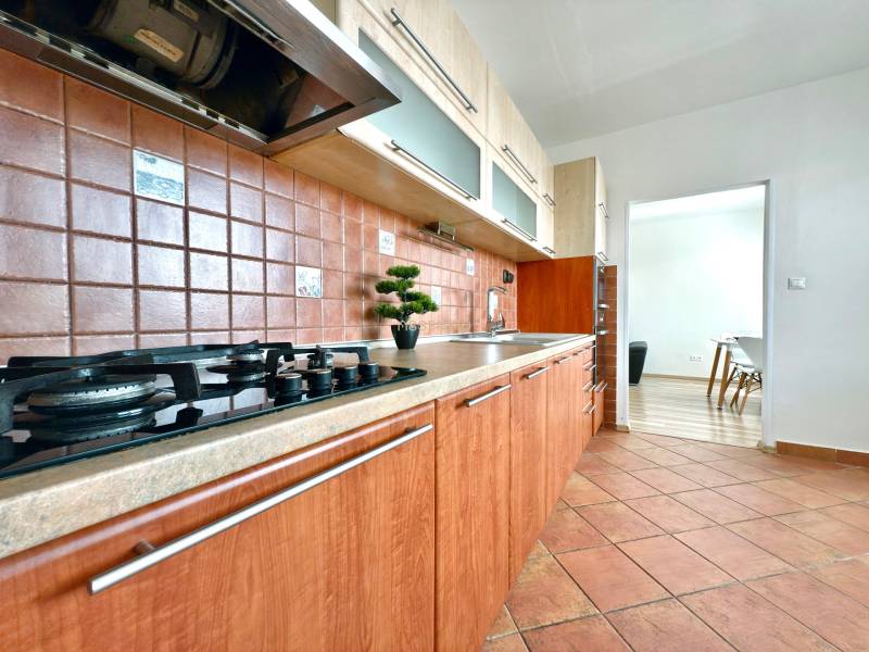 A kitchen with a gas stove, wooden cabinets, and brown tiles in a 3-room apartment.
