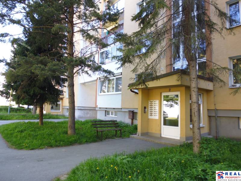Entrance to the apartment building on Karpatská Street, Prešov, surrounded by trees.