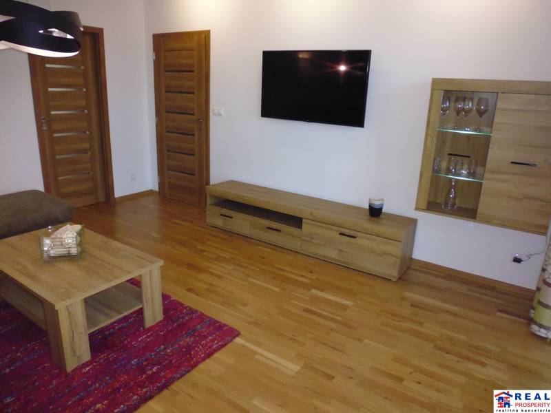 Living room in a 3-room apartment with wooden flooring, furniture, and a TV on the wall.