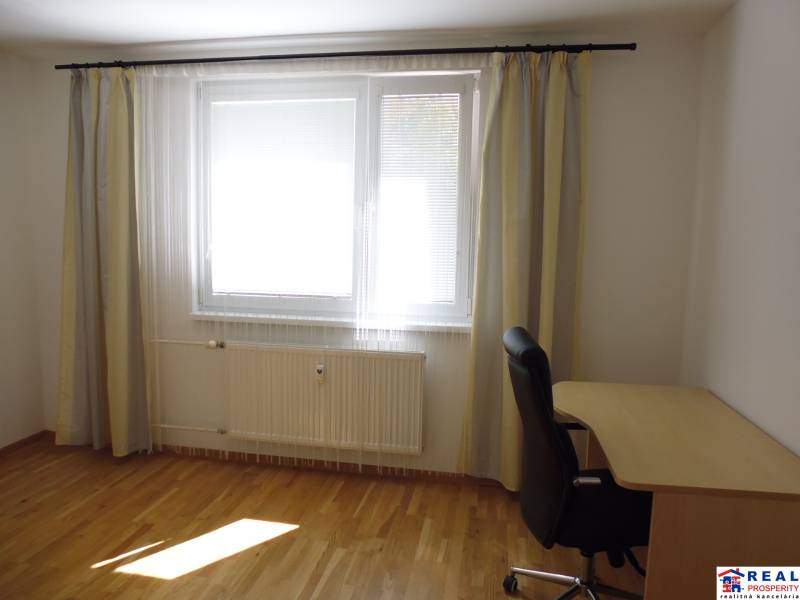 A room in a 3-room apartment with a wooden floor, a table, and a chair.
