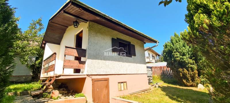 A cottage in Mojš with a garden, surrounded by trees and a clear blue sky.