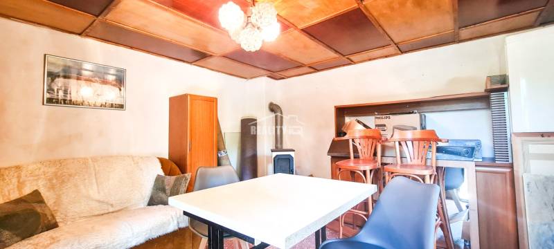 The interior of a cabin with a seating area, table, chairs, and wooden paneling on the ceiling.