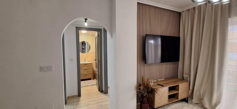 Living room in a 3-room apartment with a TV, wooden wall, and curtains.