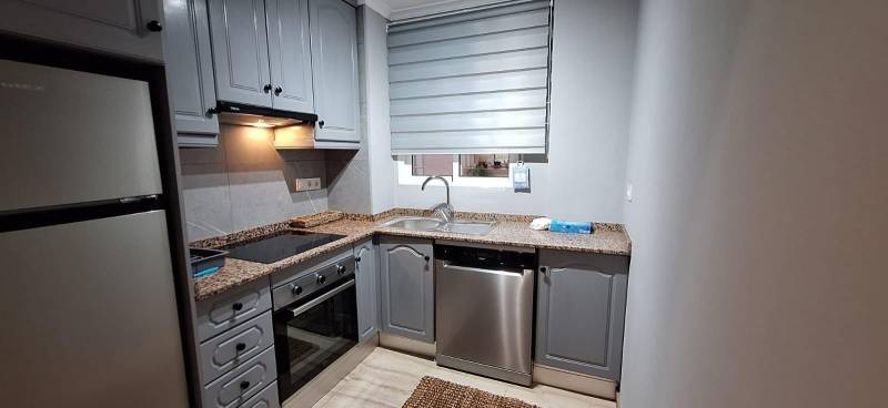 A kitchen in a 3-room apartment with a gray kitchen unit and stainless steel appliances.
