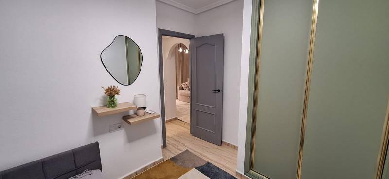 A hallway of a 3-room apartment with shelves, a mirror, and open doors.