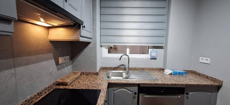 A kitchen in a 3-room apartment with a granite countertop and gray cabinets.