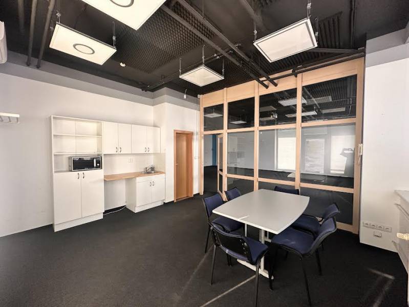 Office with a desk and chairs, kitchenette, and glass partition.