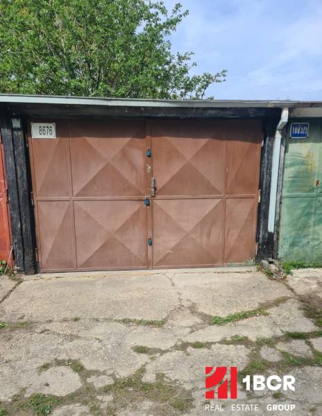 A garage in Hagarov with brown doors and the number 8676, surrounded by greenery.