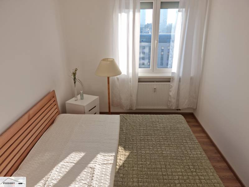 A bedroom with a bed, a lamp, and a table in a two-room apartment, large window.