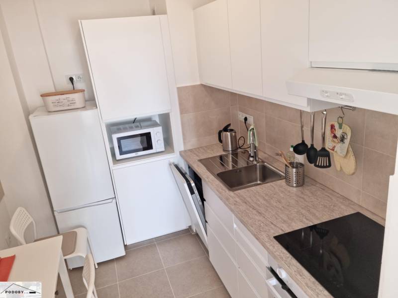 Kitchen in a 2-room apartment with a white kitchen unit, appliances, and a sink.