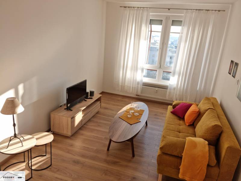Living room in a two-room apartment with a yellow sofa, TV stand, and wooden tables.