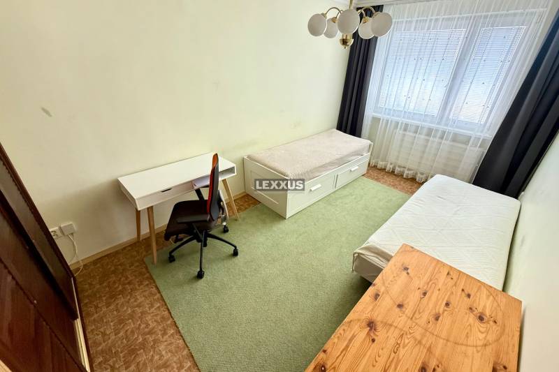 A room with two beds, a desk, and a chair in a 3-room apartment.